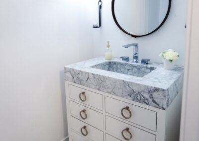 Downstairs powder room, featuring a white vanity with about 6 inches of marble on top for the sink basin. A circular mirror sits above it.