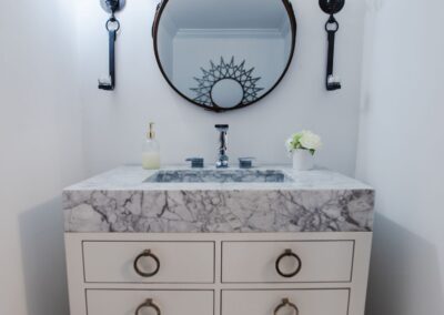 Downstairs powder room, featuring a white vanity with about 6 inches of marble on top for the sink basin. A circular mirror sits above it.