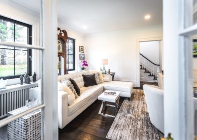 A view of the large living room featuring a sectional white couch with a large grandfather clock behind it, looking in from the sun room.