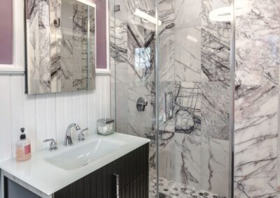 A secondary bathroom, with light purple painted walls that match the hint of purple in the quartzite that makes up the shower walls. Also included is the vanity sink with black cabinetry.