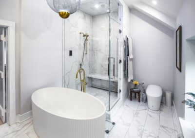 A bright white primary bathroom with a large standalone tub, a walk-in shower with brass hardware, and a bidet.