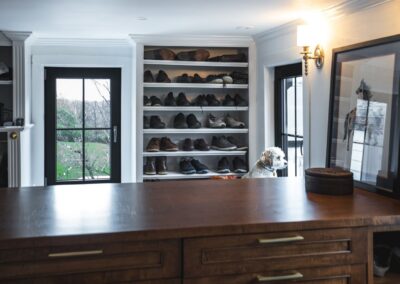 A large walk-in closet with a large wooden shelf displaying a variety of shoes. The shoes are arranged in multiple rows.